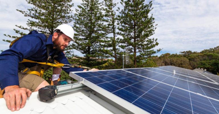 Solar panel technician with drill installing solar panels on roof